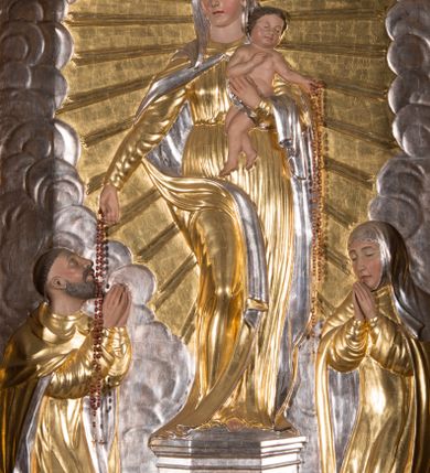 Zdjęcie nr 7: Nastawa architektoniczna, jednokondygnacyjna ze zwieńczeniem, ustawiona na dwustrefowym cokole, w górnej strefie z wyłamanymi, zdwojonymi prostopadłościanami. Ołtarz drewniany, prostopadłościenny, z drewnianą mensą. Antepedium ujęte profilowaną ramą, w polu na pomarańczowym tle namalowana korona otwarta z różańcem nad symetrycznie umieszczonymi liśćmi, z napisem „Królowo różańca świętego módl się za nami”. Nastawa ujęta parą kolumn o skręconych trzonach podzielonych na dwie strefy i kapitelach kompozytowych, ustawionych na tle wyłamanych ścianek bocznych nastawy. Podpory dźwigają pełne belkowanie, częściowo przerwane nad polem środkowym, wyłamane na ich osi. Na belkowaniu ustawione figury aniołów z arma Christi. Pole centralne wypełnione wnęką w formie stojącego prostokąta o ściętych górnych narożach, ujęte profilowaną ramą, z płaskorzeźbą Matki Boskiej Różańcowej. Wnęka flankowana ornamentem roślinnym, w przyłuczach dwa putta. Kondygnacja ujęta uszami utworzonymi z akantu i wstęgi. Zwieńczenie w formie leżącego prostokąta. W polu obraz Chrystusa w Ogrójcu o kształcie zbliżonym do kwadratu, ujęty profilowaną ramą. Obraz flankują figury św. Marii Magdaleny i św. Weroniki, nad którymi znajdują się baldachimy ze stylizowanym lambrekinem. Całość zwieńczona płaskorzeźbą tronującego Boga Ojca pośród obłoków i uskrzydlonych główek anielskich, w glorii promienistej. Struktura polichromowana w kolorze białym, profile złocone, kolumny, ornamentyka złocone i srebrzone. 


