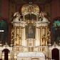 Zdjęcie nr 1: Nastawa architektoniczna, jednokondygnacyjna ze zwieńczeniem, jednoosiowa z bramkami, ustawiona na dwustrefowym cokole, z wyłamanymi pod kątem dwiema parami prostopadłościanów w górnej strefie. Ołtarz kamienny, prostopadłościenny, w drewnianej obudowie, z drewnianą mensą. Antepedium ujęte profilowaną ramą, w centrum medalion z krzyżem o trójlistnym zakończeniu ramion i promieniami na ich skrzyżowaniu, po bokach monogramy maryjny i IHS. Na ołtarzu tabernakulum z tronem wystawienia. Nastawa ujęta dwiema parami kolumn, przedzielonych dwiema parami filarów o kanelowanych trzonach, ustawionych pod kątem. Podpory dźwigają pełne belkowanie, wyłamane pod kątem na ich osi, przerwane nad polem środkowym oraz fragmenty przerwanego, półkolistego przyczółka z siedzącymi na nich puttami. Pomiędzy kolumnami ustawione figury św. Piotra i św. Pawła. W polu środkowym wnęka z obrazem św. Klemensa w formie stojącego prostokąta zakończona łukiem segmentowym z uskokiem, ujęta profilowaną ramą zwieńczoną dwiema zwróconymi ku sobie wolutami, podtrzymującymi koronę otwartą, flankowaną przez dwa putta. Kondygnacja ujęta uszami utworzonymi z suchego akantu i wstęgi. Zwieńczenie o kształcie zbliżonym do leżącego prostokąta, zamkniętego fragmentem segmentowo wyłamanego gzymsu, flankowanego spływami wolutowymi. Całe pole wypełnia obraz Zwiastowania, ujęty liśćmi. Zwieńczenie zakończone płaskorzeźbionym przedstawieniem Trójcy Świętej pośród obłoków i uskrzydlonych główek anielskich, w glorii promienistej. Bramki flankowane pilastrami o kanelowanych trzonach, podtrzymującymi nadproże wyłamane na kształt łuku kotarowego, zwieńczone kluczami z puttami. Na osi pilastrów ustawione po dwa wazony. Przejścia w formie stojącego prostokąta zamkniętego łukiem segmentowym nadwieszonym. Struktura polichromowana w kolorze białym; kolumny, profile i ornamentyka złocone, detal srebrzony. Z tyłu ołtarza ryta inskrypcja: „I.L.O.Z / 9/5 1845”.