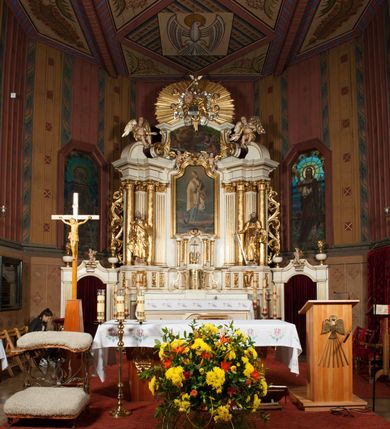 Zdjęcie nr 4: Nastawa architektoniczna, jednokondygnacyjna ze zwieńczeniem, jednoosiowa z bramkami, ustawiona na dwustrefowym cokole, z wyłamanymi pod kątem dwiema parami prostopadłościanów w górnej strefie. Ołtarz kamienny, prostopadłościenny, w drewnianej obudowie, z drewnianą mensą. Antepedium ujęte profilowaną ramą, w centrum medalion z krzyżem o trójlistnym zakończeniu ramion i promieniami na ich skrzyżowaniu, po bokach monogramy maryjny i IHS. Na ołtarzu tabernakulum z tronem wystawienia. Nastawa ujęta dwiema parami kolumn, przedzielonych dwiema parami filarów o kanelowanych trzonach, ustawionych pod kątem. Podpory dźwigają pełne belkowanie, wyłamane pod kątem na ich osi, przerwane nad polem środkowym oraz fragmenty przerwanego, półkolistego przyczółka z siedzącymi na nich puttami. Pomiędzy kolumnami ustawione figury św. Piotra i św. Pawła. W polu środkowym wnęka z obrazem św. Klemensa w formie stojącego prostokąta zakończona łukiem segmentowym z uskokiem, ujęta profilowaną ramą zwieńczoną dwiema zwróconymi ku sobie wolutami, podtrzymującymi koronę otwartą, flankowaną przez dwa putta. Kondygnacja ujęta uszami utworzonymi z suchego akantu i wstęgi. Zwieńczenie o kształcie zbliżonym do leżącego prostokąta, zamkniętego fragmentem segmentowo wyłamanego gzymsu, flankowanego spływami wolutowymi. Całe pole wypełnia obraz Zwiastowania, ujęty liśćmi. Zwieńczenie zakończone płaskorzeźbionym przedstawieniem Trójcy Świętej pośród obłoków i uskrzydlonych główek anielskich, w glorii promienistej. Bramki flankowane pilastrami o kanelowanych trzonach, podtrzymującymi nadproże wyłamane na kształt łuku kotarowego, zwieńczone kluczami z puttami. Na osi pilastrów ustawione po dwa wazony. Przejścia w formie stojącego prostokąta zamkniętego łukiem segmentowym nadwieszonym. Struktura polichromowana w kolorze białym; kolumny, profile i ornamentyka złocone, detal srebrzony. Z tyłu ołtarza ryta inskrypcja: „I.L.O.Z / 9/5 1845”.