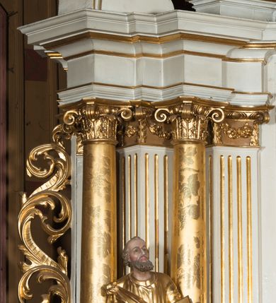 Zdjęcie nr 18: Nastawa architektoniczna, jednokondygnacyjna ze zwieńczeniem, jednoosiowa z bramkami, ustawiona na dwustrefowym cokole, z wyłamanymi pod kątem dwiema parami prostopadłościanów w górnej strefie. Ołtarz kamienny, prostopadłościenny, w drewnianej obudowie, z drewnianą mensą. Antepedium ujęte profilowaną ramą, w centrum medalion z krzyżem o trójlistnym zakończeniu ramion i promieniami na ich skrzyżowaniu, po bokach monogramy maryjny i IHS. Na ołtarzu tabernakulum z tronem wystawienia. Nastawa ujęta dwiema parami kolumn, przedzielonych dwiema parami filarów o kanelowanych trzonach, ustawionych pod kątem. Podpory dźwigają pełne belkowanie, wyłamane pod kątem na ich osi, przerwane nad polem środkowym oraz fragmenty przerwanego, półkolistego przyczółka z siedzącymi na nich puttami. Pomiędzy kolumnami ustawione figury św. Piotra i św. Pawła. W polu środkowym wnęka z obrazem św. Klemensa w formie stojącego prostokąta zakończona łukiem segmentowym z uskokiem, ujęta profilowaną ramą zwieńczoną dwiema zwróconymi ku sobie wolutami, podtrzymującymi koronę otwartą, flankowaną przez dwa putta. Kondygnacja ujęta uszami utworzonymi z suchego akantu i wstęgi. Zwieńczenie o kształcie zbliżonym do leżącego prostokąta, zamkniętego fragmentem segmentowo wyłamanego gzymsu, flankowanego spływami wolutowymi. Całe pole wypełnia obraz Zwiastowania, ujęty liśćmi. Zwieńczenie zakończone płaskorzeźbionym przedstawieniem Trójcy Świętej pośród obłoków i uskrzydlonych główek anielskich, w glorii promienistej. Bramki flankowane pilastrami o kanelowanych trzonach, podtrzymującymi nadproże wyłamane na kształt łuku kotarowego, zwieńczone kluczami z puttami. Na osi pilastrów ustawione po dwa wazony. Przejścia w formie stojącego prostokąta zamkniętego łukiem segmentowym nadwieszonym. Struktura polichromowana w kolorze białym; kolumny, profile i ornamentyka złocone, detal srebrzony. Z tyłu ołtarza ryta inskrypcja: „I.L.O.Z / 9/5 1845”.