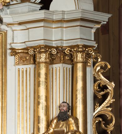 Zdjęcie nr 19: Nastawa architektoniczna, jednokondygnacyjna ze zwieńczeniem, jednoosiowa z bramkami, ustawiona na dwustrefowym cokole, z wyłamanymi pod kątem dwiema parami prostopadłościanów w górnej strefie. Ołtarz kamienny, prostopadłościenny, w drewnianej obudowie, z drewnianą mensą. Antepedium ujęte profilowaną ramą, w centrum medalion z krzyżem o trójlistnym zakończeniu ramion i promieniami na ich skrzyżowaniu, po bokach monogramy maryjny i IHS. Na ołtarzu tabernakulum z tronem wystawienia. Nastawa ujęta dwiema parami kolumn, przedzielonych dwiema parami filarów o kanelowanych trzonach, ustawionych pod kątem. Podpory dźwigają pełne belkowanie, wyłamane pod kątem na ich osi, przerwane nad polem środkowym oraz fragmenty przerwanego, półkolistego przyczółka z siedzącymi na nich puttami. Pomiędzy kolumnami ustawione figury św. Piotra i św. Pawła. W polu środkowym wnęka z obrazem św. Klemensa w formie stojącego prostokąta zakończona łukiem segmentowym z uskokiem, ujęta profilowaną ramą zwieńczoną dwiema zwróconymi ku sobie wolutami, podtrzymującymi koronę otwartą, flankowaną przez dwa putta. Kondygnacja ujęta uszami utworzonymi z suchego akantu i wstęgi. Zwieńczenie o kształcie zbliżonym do leżącego prostokąta, zamkniętego fragmentem segmentowo wyłamanego gzymsu, flankowanego spływami wolutowymi. Całe pole wypełnia obraz Zwiastowania, ujęty liśćmi. Zwieńczenie zakończone płaskorzeźbionym przedstawieniem Trójcy Świętej pośród obłoków i uskrzydlonych główek anielskich, w glorii promienistej. Bramki flankowane pilastrami o kanelowanych trzonach, podtrzymującymi nadproże wyłamane na kształt łuku kotarowego, zwieńczone kluczami z puttami. Na osi pilastrów ustawione po dwa wazony. Przejścia w formie stojącego prostokąta zamkniętego łukiem segmentowym nadwieszonym. Struktura polichromowana w kolorze białym; kolumny, profile i ornamentyka złocone, detal srebrzony. Z tyłu ołtarza ryta inskrypcja: „I.L.O.Z / 9/5 1845”.