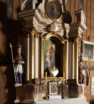 Zdjęcie nr 2: Nastawa architektoniczna, jednoosiowa, jednokondygnacyjna ze zwieńczeniem, ustawiona na dwustrefowym cokole, w górnej części z wyłamanymi pod kątem dwoma prostopadłościanami. Ołtarz drewniany, prostopadłościenny, skrzyniowy, z drewnianą mensą. Antepedium ujęte profilowaną ramą, w polu dwie duże, płaskorzeźbione rozety na pomarańczowym tle. Nastawa ujęta parą kolumn ustawionych na tle pilastrów, dźwigających pełne belkowanie, wyłamane pod kątem na ich osi, częściowo przerwane nad polem środkowym oraz fragmenty przerwanego półkolistego przyczółka. Pole centralne w całości wypełnione wnęką w formie stojącego prostokąta zamkniętego łukiem segmentowym nadwieszonym, ujętym profilowaną ramą, z obrazem św. Antoniego Padewskiego. Nad nim akantowy kartusz, z przedstawieniem dwóch skrzyżowanych kluczy w polu. Kondygnację flankują dwie figury biskupów ustawione na wysuniętych krawędziach cokołu oraz uszy utworzone z suchego akantu i wstęgi. Zwieńczenie w formie zbliżonej do trapezu zamkniętego fragmentem gzymsu o kształcie łuku segmentowego z uskokiem, flankowanego spływami wolutowymi. W polu obraz św. Antoniego Padewskiego w formie stojącego owalu, ujęty profilowaną ramą, u góry dekorowany zwisami kwiatowymi, u dołu liśćmi. Całość zakończona figurką św. Michała Archanioła trzymającego w uniesionej ręce miecz. Struktura polichromowana w kolorze białym; kolumny, profile i ornamentyka złocone, detal srebrzony. 


