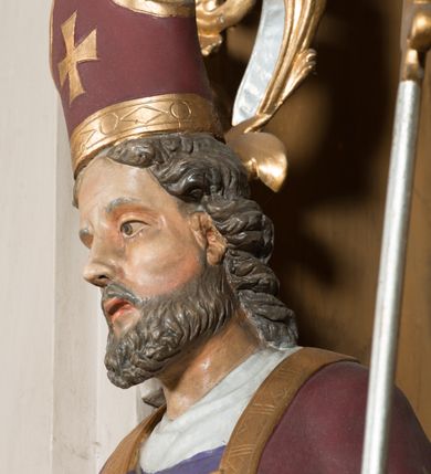 Zdjęcie nr 14: Nastawa architektoniczna, jednoosiowa, jednokondygnacyjna ze zwieńczeniem, ustawiona na dwustrefowym cokole, w górnej części z wyłamanymi pod kątem dwoma prostopadłościanami. Ołtarz drewniany, prostopadłościenny, skrzyniowy, z drewnianą mensą. Antepedium ujęte profilowaną ramą, w polu dwie duże, płaskorzeźbione rozety na pomarańczowym tle. Nastawa ujęta parą kolumn ustawionych na tle pilastrów, dźwigających pełne belkowanie, wyłamane pod kątem na ich osi, częściowo przerwane nad polem środkowym oraz fragmenty przerwanego półkolistego przyczółka. Pole centralne w całości wypełnione wnęką w formie stojącego prostokąta zamkniętego łukiem segmentowym nadwieszonym, ujętym profilowaną ramą, z obrazem św. Antoniego Padewskiego. Nad nim akantowy kartusz, z przedstawieniem dwóch skrzyżowanych kluczy w polu. Kondygnację flankują dwie figury biskupów ustawione na wysuniętych krawędziach cokołu oraz uszy utworzone z suchego akantu i wstęgi. Zwieńczenie w formie zbliżonej do trapezu zamkniętego fragmentem gzymsu o kształcie łuku segmentowego z uskokiem, flankowanego spływami wolutowymi. W polu obraz św. Antoniego Padewskiego w formie stojącego owalu, ujęty profilowaną ramą, u góry dekorowany zwisami kwiatowymi, u dołu liśćmi. Całość zakończona figurką św. Michała Archanioła trzymającego w uniesionej ręce miecz. Struktura polichromowana w kolorze białym; kolumny, profile i ornamentyka złocone, detal srebrzony. 


