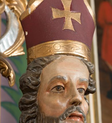 Zdjęcie nr 15: Nastawa architektoniczna, jednoosiowa, jednokondygnacyjna ze zwieńczeniem, ustawiona na dwustrefowym cokole, w górnej części z wyłamanymi pod kątem dwoma prostopadłościanami. Ołtarz drewniany, prostopadłościenny, skrzyniowy, z drewnianą mensą. Antepedium ujęte profilowaną ramą, w polu dwie duże, płaskorzeźbione rozety na pomarańczowym tle. Nastawa ujęta parą kolumn ustawionych na tle pilastrów, dźwigających pełne belkowanie, wyłamane pod kątem na ich osi, częściowo przerwane nad polem środkowym oraz fragmenty przerwanego półkolistego przyczółka. Pole centralne w całości wypełnione wnęką w formie stojącego prostokąta zamkniętego łukiem segmentowym nadwieszonym, ujętym profilowaną ramą, z obrazem św. Antoniego Padewskiego. Nad nim akantowy kartusz, z przedstawieniem dwóch skrzyżowanych kluczy w polu. Kondygnację flankują dwie figury biskupów ustawione na wysuniętych krawędziach cokołu oraz uszy utworzone z suchego akantu i wstęgi. Zwieńczenie w formie zbliżonej do trapezu zamkniętego fragmentem gzymsu o kształcie łuku segmentowego z uskokiem, flankowanego spływami wolutowymi. W polu obraz św. Antoniego Padewskiego w formie stojącego owalu, ujęty profilowaną ramą, u góry dekorowany zwisami kwiatowymi, u dołu liśćmi. Całość zakończona figurką św. Michała Archanioła trzymającego w uniesionej ręce miecz. Struktura polichromowana w kolorze białym; kolumny, profile i ornamentyka złocone, detal srebrzony. 


