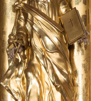 Zdjęcie nr 3: Figura drążona z tyłu, ustawiona na nieregularnej podstawie. Święty ukazany frontalnie, z uniesioną głową, prawą nogą opartą na wzniesieniu i rękami rozłożonymi na boki. W prawej dłoni trzyma dwa skrzyżowane klucze, lewą podtrzymuje zamkniętą księgę. Twarz ma szczupłą, pociągłą, o głęboko osadzonych oczach, skierowanych w górę, garbatym nosie i otwartych ustach z widoczną linią zębów. Twarz okolona krótką, falowaną brodą oraz krótkimi włosami, z łysiną na głowie. Ubrany jest w luźną, złoconą tunikę oraz zawiązany diagonalnie na prawym ramieniu złocony płaszcz. Polichromia naturalistyczna w partiach ciała, włosy siwo-brązowe. 

