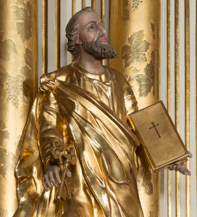 Zdjęcie nr 1: Figura drążona z tyłu, ustawiona na nieregularnej podstawie. Święty ukazany frontalnie, z uniesioną głową, prawą nogą opartą na wzniesieniu i rękami rozłożonymi na boki. W prawej dłoni trzyma dwa skrzyżowane klucze, lewą podtrzymuje zamkniętą księgę. Twarz ma szczupłą, pociągłą, o głęboko osadzonych oczach, skierowanych w górę, garbatym nosie i otwartych ustach z widoczną linią zębów. Twarz okolona krótką, falowaną brodą oraz krótkimi włosami, z łysiną na głowie. Ubrany jest w luźną, złoconą tunikę oraz zawiązany diagonalnie na prawym ramieniu złocony płaszcz. Polichromia naturalistyczna w partiach ciała, włosy siwo-brązowe. 

