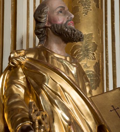 Zdjęcie nr 5: Figura drążona z tyłu, ustawiona na nieregularnej podstawie. Święty ukazany frontalnie, z uniesioną głową, prawą nogą opartą na wzniesieniu i rękami rozłożonymi na boki. W prawej dłoni trzyma dwa skrzyżowane klucze, lewą podtrzymuje zamkniętą księgę. Twarz ma szczupłą, pociągłą, o głęboko osadzonych oczach, skierowanych w górę, garbatym nosie i otwartych ustach z widoczną linią zębów. Twarz okolona krótką, falowaną brodą oraz krótkimi włosami, z łysiną na głowie. Ubrany jest w luźną, złoconą tunikę oraz zawiązany diagonalnie na prawym ramieniu złocony płaszcz. Polichromia naturalistyczna w partiach ciała, włosy siwo-brązowe. 

