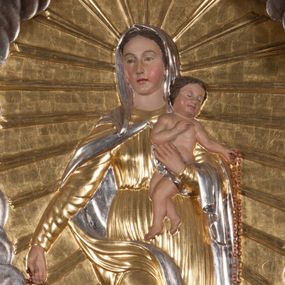 Zdjęcie nr 1: Płaskorzeźba w kształcie stojącego prostokąta o ściętych górnych narożach. W centrum kompozycji na wielobocznym cokole z rytą datą „1872” stoi Maria, ukazana frontalnie, w kontrapoście, lewą ręką podtrzymuje Dzieciątko, prawą wyciąga w bok, w dłoni trzyma różaniec. Twarz ma owalną, o łagodnych rysach, migdałowatych oczach, prostym nosie i pełnych ustach, okoloną brązowymi włosami ukrytymi pod welonem. Ubrana jest w przylegającą do ciała, obficie drapowaną suknię, przepasaną w talii, pod szyją ma zapięty płaszcz opadający na ramiona i prawą nogę, a na głowie welon. Dzieciątko w pozycji siedzącej, o esowato wygiętej sylwetce, zwrócone w lewo, prawą rękę ugina i unosi w geście błogosławieństwa, lewą wyciąga przed siebie, w dłoni trzyma różaniec. Twarz ma kwadratową, o pełnych policzkach, zamkniętych oczach, małym nosie i ustach, okoloną krótkimi, brązowymi włosami. Ciało ma pulchne, w partii bioder przewiązane pieluszką. W lewym dolnym rogu obrazu klęcząca postać św. Dominika, ukazana z prawego profilu, z uniesioną głową i rękami złożonymi w geście modlitwy. Twarz ma szczupłą, z oczami skierowanymi w górę, okoloną krótką brodą i włosami, na głowie ma tonsurę. Ubrany jest w habit ze szkaplerzem oraz płaszcz z kapturem. Przed nim, na ziemi leży pies z pochodnią w pysku. W prawym dolnym rogu klęcząca św. Katarzyna Sieneńska, zwrócona w trzech czwartych do środka kompozycji, z dłońmi złożonymi w geście modlitwy. Twarz ma pociągłą, o zamkniętych oczach, długim nosie i wąskich ustach. Wokół głowy ma podwikę, na niej welon. Ubrana jest w habit ze szkaplerzem, na ramiona ma narzucony płaszcz. Wokół Marii gloria promienista, tło przedstawienia wypełnione obłokami. Polichromia w partiach ciała naturalistyczna, stroje i tło złocone i srebrzone. 