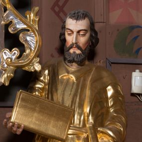 Zdjęcie nr 1: Figura pełnoplastyczna, ustawiona na nieregularnej podstawie. Święty ukazany frontalnie, z lekko pochyloną głową. W prawej, ugiętej ręce trzyma zamkniętą księgę, w lewej pałkę. Twarz ma pociągłą, o dojrzałych rysach, zmarszczonym czole, półprzymkniętych oczach, prostym nosie i pełnych ustach, okoloną krótką, falistą brodą i włosami. Ubrany jest w złoconą tunikę z kołnierzykiem, przepasaną w talii, przylegającą do ciała, silnie drapowaną oraz płaszcz zarzucony na prawe ramię postaci i opadający po bokach. Polichromia ciała naturalistyczna, włosy brązowe. 

