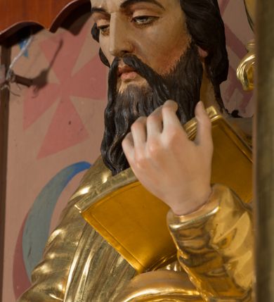 Zdjęcie nr 3: Figura pełnoplastyczna ustawiona na nieregularnej podstawie. Święty ukazany frontalnie, z pochyloną głową, lewą nogą ugiętą, opartą na podstawie. Lewą ręką podtrzymuje otwartą księgę, prawą wyciąga w bok i opiera na pile. Twarz ma pociągłą, o dojrzałych rysach, zmarszczonym czole, półprzymkniętych oczach, prostym nosie i pełnych ustach, okoloną długą, rozdwajającą się brodą i krótkimi, falowanymi włosami. Ubrany jest w złoconą tunikę, przylegającą do ciała, obficie drapowaną, przepasaną w talii oraz płaszcz zarzucony na ramiona i na lewy bok postaci. Polichromia ciała naturalistyczna, włosy brązowe. 
