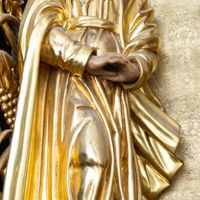 Zdjęcie nr 1: Rzeźba drążona, przedstawiająca Matkę Boską, ustawiona na niskim i półkolistym cokole. Maria zwrócona delikatnie w lewo, w kontrapoście z prawą nogą ugiętą w kolanie i z dłońmi splecionymi poniżej pasa. Twarz okrągła z wyraźnie zaznaczonym podbródkiem, małymi ustami i dużym, prostym nosem. Włosy długie, częściowo schowane pod welonem, ciemnobrązowe, opadające na plecy. Matka Boska jest ubrana w długą suknię z długimi rękawami, przewiązaną pasem oraz płaszcz, założony na głowę, na stopach ma pełne buty. Draperia szat gęsta, równolegle biegnąca w dół. Polichromia w odsłoniętych partiach ciała naturalistyczna, ubiór złocony.

