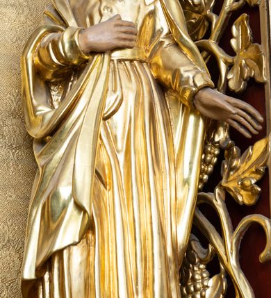 Zdjęcie nr 1: Rzeźba drążona, przedstawiająca św. Jana Ewangelistę, ustawiona na niskim, półkolistym cokole. Święty zwrócony delikatnie w prawo, w kontrapoście, z głową skierowaną w prawo i uniesioną nieco do góry, z prawą ręką złożoną na piersi, a lewą wyprostowaną i odsuniętą w bok. Twarz okrągła z wyraźnie zaznaczonym podbródkiem, małymi ustami i prostym nosem; włosy długie, ciemnobrązowe z przedziałkiem pośrodku, opadające na plecy. Święty jest ubrany w długą szatę z długimi rękawami, zapiętą w górnej części na guziki, przewiązaną pasem oraz płaszcz, którego jeden koniec trzyma w prawej dłoni. Draperia szat gęsta, równolegle biegnąca w dół. Polichromia w odsłoniętych partiach ciała naturalistyczna, szaty złocone.

