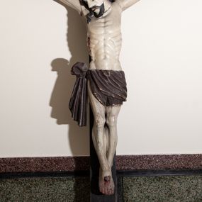 Zdjęcie nr 1: Rzeźba Chrystusa przybita do krzyża trzema gwoździami, pełna. Zbawiciel ukazany w typie Cristo vivo, w lekkim zwisie, z głową pochyloną na prawą stronę. Chrystus ma szczupłą sylwetkę ciała, delikatnie podkreśloną linię żeber. Jego twarz jest podłużna, ma długi nos, delikatnie otwarte usta i oczy, krótką brodę. Ma długie, brązowe włosy spływające na plecy i prawe ramię, a na głowie założoną koronę cierniową złożoną z dwóch gałązek. Biodra oplata brązowe perizonium, zawiązane na prawym boku z jednym końcem zwisającym wzdłuż prawego uda. Z dłoni, stóp i boku Chrystusa spływają strużki krwi. Polichromia ciała naturalistyczna, krzyż brązowy. 