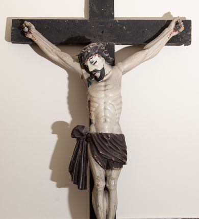 Zdjęcie nr 3: Rzeźba Chrystusa przybita do krzyża trzema gwoździami, pełna. Zbawiciel ukazany w typie Cristo vivo, w lekkim zwisie, z głową pochyloną na prawą stronę. Chrystus ma szczupłą sylwetkę ciała, delikatnie podkreśloną linię żeber. Jego twarz jest podłużna, ma długi nos, delikatnie otwarte usta i oczy, krótką brodę. Ma długie, brązowe włosy spływające na plecy i prawe ramię, a na głowie założoną koronę cierniową złożoną z dwóch gałązek. Biodra oplata brązowe perizonium, zawiązane na prawym boku z jednym końcem zwisającym wzdłuż prawego uda. Z dłoni, stóp i boku Chrystusa spływają strużki krwi. Polichromia ciała naturalistyczna, krzyż brązowy. 