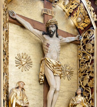 Zdjęcie nr 1: Rzeźba Chrystusa przybita do krzyża trzema gwoździami. Chrystus ukazany w typie Cristo morte, w lekkim zwisie, z głową pochyloną na prawą stronę. Ma szczupłą sylwetkę ciała, podkreśloną linię żeber i mostka. Jego twarz jest podłużna, ma długi nos, otwarte usta i zamknięte oczy oraz krótką brodę. Włosy długie, ciemnobrązowe, spływają falami do przodu i na plecy. Na głowie ma założoną szeroką, złoconą koronę cierniową. Jego biodra oplata złocone perizonium, zawiązane na prawym boku ze zwisem wzdłuż prawego uda. Z dłoni, stóp i boku Chrystusa spływają strużki krwi. Nad głową wisi titulus w formie poziomej banderoli z napisem „I. N. R. I.”. Krzyż prosty, gładki, malowany na brązowo. Polichromia ciała naturalistyczna; perizonium, korona i titulus złocone.





