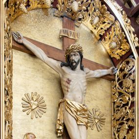 Zdjęcie nr 1: Rzeźba Chrystusa przybita do krzyża trzema gwoździami. Chrystus ukazany w typie Cristo morte, w lekkim zwisie, z głową pochyloną na prawą stronę. Ma szczupłą sylwetkę ciała, podkreśloną linię żeber i mostka. Jego twarz jest podłużna, ma długi nos, otwarte usta i zamknięte oczy oraz krótką brodę. Włosy długie, ciemnobrązowe, spływają falami do przodu i na plecy. Na głowie ma założoną szeroką, złoconą koronę cierniową. Jego biodra oplata złocone perizonium, zawiązane na prawym boku ze zwisem wzdłuż prawego uda. Z dłoni, stóp i boku Chrystusa spływają strużki krwi. Nad głową wisi titulus w formie poziomej banderoli z napisem „I. N. R. I.”. Krzyż prosty, gładki, malowany na brązowo. Polichromia ciała naturalistyczna; perizonium, korona i titulus złocone.





