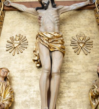 Zdjęcie nr 3: Rzeźba Chrystusa przybita do krzyża trzema gwoździami. Chrystus ukazany w typie Cristo morte, w lekkim zwisie, z głową pochyloną na prawą stronę. Ma szczupłą sylwetkę ciała, podkreśloną linię żeber i mostka. Jego twarz jest podłużna, ma długi nos, otwarte usta i zamknięte oczy oraz krótką brodę. Włosy długie, ciemnobrązowe, spływają falami do przodu i na plecy. Na głowie ma założoną szeroką, złoconą koronę cierniową. Jego biodra oplata złocone perizonium, zawiązane na prawym boku ze zwisem wzdłuż prawego uda. Z dłoni, stóp i boku Chrystusa spływają strużki krwi. Nad głową wisi titulus w formie poziomej banderoli z napisem „I. N. R. I.”. Krzyż prosty, gładki, malowany na brązowo. Polichromia ciała naturalistyczna; perizonium, korona i titulus złocone.





