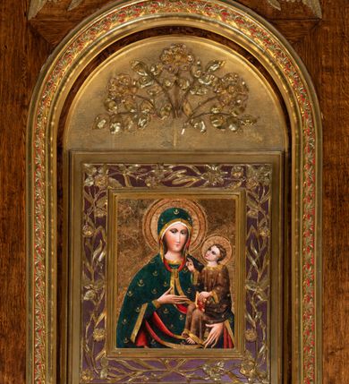 Zdjęcie nr 13: Obraz w kształcie stojącego prostokąta. W centrum kompozycji Matka Boska w typie Hodegetrii ukazana w półpostaci, frontalnie z Dzieciątkiem Jezus na lewym reku, prawą na nie wskazująca. Twarz Marii pociągła, z długim nosem, małymi ustami, ciemnobrązowymi oczami o ciemnej karnacji z zarumienionymi policzkami. Matka Boska ubrana jest w czerwoną suknię ze złotą lamówką przy szyi oraz niebieski płaszcz z motywami kwiatowymi i złotą lamówką na brzegu, zarzucony na ramiona i głowę, zawiązany na piersi wstążką w kokardkę. Dzieciątko ukazane w całej postaci, zwrócone trzy czwarte w prawo, lewą ręką podtrzymuje złotą księgę, prawą unosi na wysokości piersi w geście błogosławieństwa. Twarz okrągła z długim nosem, wąskimi ustami, półprzymkniętymi oczami, okolona krótkimi i brązowymi włosami. Jezus ubrany jest w szarą suknię z długimi rękawami, zdobioną żółto-niebieskim ornamentem kwiatowym oraz złote sandały. Głowy obu postaci ujmują złocone promieniste nimby, otoczone złotym okręgiem. Na głowie Marii i Dzieciątka złote korony: korona Dzieciątka zamknięta, korona Marii widoczna do połowy. Tło złote, ryte w ornamenty roślinne. Rama podwójna: wewnętrzna złocona i profilowana, a zewnętrzna ozdobiona rzeźbioną dekoracją roślinną na czerwonym tle, na brzegach złocona i profilowana.