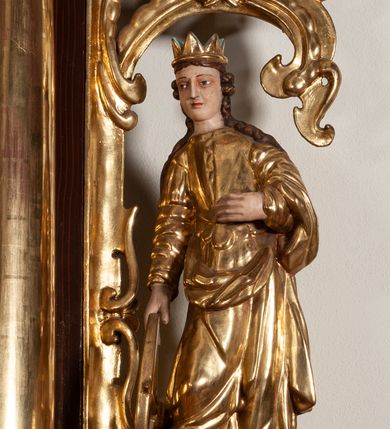 Zdjęcie nr 20: Ołtarz architektoniczny, dwukondygnacyjny, jednoosiowy ze zwieńczeniem. Mensa prostopadłościenna, antepedium w kształcie leżącego prostokąta, flankowane dwoma kanelowanymi pilastrami. W polu, w złoconej ramie dwie połączone płyciny w kształcie stojącego prostokąta wypełnione symetryczną dekoracją z akantu na błękitnym tle. Tabernakulum w formie prostopadłościennej, marmurowej skrzynki, zamknięte od góry prostym, złoconym gzymsem. Ścianka frontowa i drzwiczki obwiedzione złoconymi listwami, w polu łaciński krzyż. Cokół nastawy ustawiony na jednym stopniu, pośrodku zdobiony płyciną w kształcie leżącego prostokąta o zaokrąglonych krótszych bokach, imposty dekorowane mniejszymi płycinami wypełnionymi dekoracją roślinną. Pierwsza kondygnacja ujęta parą kolumn dźwigających przerwane belkowanie z przyczółkami, po bokach dodatkowo flankowana uszami wykończonymi ornamentem małżowinowo-chrząstkowym. W polu głównym obraz Matki Boskiej Szkaplerznej oraz św. Józefa z Dzieciątkiem i ze św. Janem Chrzcicielem na zasuwie, nad nimi para, małych uskrzydlonych aniołków. Po bokach nastawy dwie rzeźby: po prawej św. Katarzyna Aleksandryjska, a po lewej św. Barbara. Na przyczółkach usadzone dwie rzeźby aniołów z rozłożonymi szeroko rękami. Kolumny ustawione na tle prostokątnych płycin, z bazami, trzony gładkie, kapitele kompozytowe. Druga kondygnacja flankowana parą kolumn podtrzymujących wyłamane belkowanie. W polu, w ramie o kształcie stojącego prostokąta o ściętych narożach obraz św. Katarzyny Aleksandryjskiej. W zwieńczeniu promienista gloria z monogramem Marii na błękitnym tle, obwiedzionym wieńcem z obłoków. Struktura malowana w kolorze naturalnego drewna, ornamentyka złocona, detale srebrzone i błękitne.

