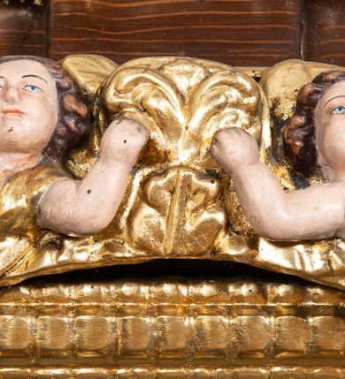 Zdjęcie nr 25: Ołtarz architektoniczny, dwukondygnacyjny, jednoosiowy ze zwieńczeniem. Mensa prostopadłościenna, antepedium w kształcie leżącego prostokąta, flankowane dwoma kanelowanymi pilastrami. W polu, w złoconej ramie dwie połączone płyciny w kształcie stojącego prostokąta wypełnione symetryczną dekoracją z akantu na błękitnym tle. Tabernakulum w formie prostopadłościennej, marmurowej skrzynki, zamknięte od góry prostym, złoconym gzymsem. Ścianka frontowa i drzwiczki obwiedzione złoconymi listwami, w polu łaciński krzyż. Cokół nastawy ustawiony na jednym stopniu, pośrodku zdobiony płyciną w kształcie leżącego prostokąta o zaokrąglonych krótszych bokach, imposty dekorowane mniejszymi płycinami wypełnionymi dekoracją roślinną. Pierwsza kondygnacja ujęta parą kolumn dźwigających przerwane belkowanie z przyczółkami, po bokach dodatkowo flankowana uszami wykończonymi ornamentem małżowinowo-chrząstkowym. W polu głównym obraz Matki Boskiej Szkaplerznej oraz św. Józefa z Dzieciątkiem i ze św. Janem Chrzcicielem na zasuwie, nad nimi para, małych uskrzydlonych aniołków. Po bokach nastawy dwie rzeźby: po prawej św. Katarzyna Aleksandryjska, a po lewej św. Barbara. Na przyczółkach usadzone dwie rzeźby aniołów z rozłożonymi szeroko rękami. Kolumny ustawione na tle prostokątnych płycin, z bazami, trzony gładkie, kapitele kompozytowe. Druga kondygnacja flankowana parą kolumn podtrzymujących wyłamane belkowanie. W polu, w ramie o kształcie stojącego prostokąta o ściętych narożach obraz św. Katarzyny Aleksandryjskiej. W zwieńczeniu promienista gloria z monogramem Marii na błękitnym tle, obwiedzionym wieńcem z obłoków. Struktura malowana w kolorze naturalnego drewna, ornamentyka złocona, detale srebrzone i błękitne.

