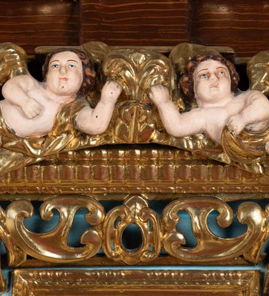 Zdjęcie nr 39: Ołtarz architektoniczny, dwukondygnacyjny, jednoosiowy ze zwieńczeniem. Mensa prostopadłościenna, antepedium w kształcie leżącego prostokąta, flankowane dwoma kanelowanymi pilastrami. W polu, w złoconej ramie dwie połączone płyciny w kształcie stojącego prostokąta wypełnione symetryczną dekoracją z akantu na błękitnym tle. Tabernakulum w formie prostopadłościennej, marmurowej skrzynki, zamknięte od góry prostym, złoconym gzymsem. Ścianka frontowa i drzwiczki obwiedzione złoconymi listwami, w polu łaciński krzyż. Cokół nastawy ustawiony na jednym stopniu, pośrodku zdobiony płyciną w kształcie leżącego prostokąta o zaokrąglonych krótszych bokach, imposty dekorowane mniejszymi płycinami wypełnionymi dekoracją roślinną. Pierwsza kondygnacja ujęta parą kolumn dźwigających przerwane belkowanie z przyczółkami, po bokach dodatkowo flankowana uszami wykończonymi ornamentem małżowinowo-chrząstkowym. W polu głównym obraz Matki Boskiej Szkaplerznej oraz św. Józefa z Dzieciątkiem i ze św. Janem Chrzcicielem na zasuwie, nad nimi para, małych uskrzydlonych aniołków. Po bokach nastawy dwie rzeźby: po prawej św. Katarzyna Aleksandryjska, a po lewej św. Barbara. Na przyczółkach usadzone dwie rzeźby aniołów z rozłożonymi szeroko rękami. Kolumny ustawione na tle prostokątnych płycin, z bazami, trzony gładkie, kapitele kompozytowe. Druga kondygnacja flankowana parą kolumn podtrzymujących wyłamane belkowanie. W polu, w ramie o kształcie stojącego prostokąta o ściętych narożach obraz św. Katarzyny Aleksandryjskiej. W zwieńczeniu promienista gloria z monogramem Marii na błękitnym tle, obwiedzionym wieńcem z obłoków. Struktura malowana w kolorze naturalnego drewna, ornamentyka złocona, detale srebrzone i błękitne.

