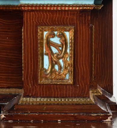 Zdjęcie nr 53: Ołtarz architektoniczny, dwukondygnacyjny, jednoosiowy ze zwieńczeniem. Mensa prostopadłościenna, antepedium w kształcie leżącego prostokąta, flankowane dwoma kanelowanymi pilastrami. W polu, w złoconej ramie dwie połączone płyciny w kształcie stojącego prostokąta wypełnione symetryczną dekoracją z akantu na błękitnym tle. Tabernakulum w formie prostopadłościennej, marmurowej skrzynki, zamknięte od góry prostym, złoconym gzymsem. Ścianka frontowa i drzwiczki obwiedzione złoconymi listwami, w polu łaciński krzyż. Cokół nastawy ustawiony na jednym stopniu, pośrodku zdobiony płyciną w kształcie leżącego prostokąta o zaokrąglonych krótszych bokach, imposty dekorowane mniejszymi płycinami wypełnionymi dekoracją roślinną. Pierwsza kondygnacja ujęta parą kolumn dźwigających przerwane belkowanie z przyczółkami, po bokach dodatkowo flankowana uszami wykończonymi ornamentem małżowinowo-chrząstkowym. W polu głównym obraz Matki Boskiej Szkaplerznej oraz św. Józefa z Dzieciątkiem i ze św. Janem Chrzcicielem na zasuwie, nad nimi para, małych uskrzydlonych aniołków. Po bokach nastawy dwie rzeźby: po prawej św. Katarzyna Aleksandryjska, a po lewej św. Barbara. Na przyczółkach usadzone dwie rzeźby aniołów z rozłożonymi szeroko rękami. Kolumny ustawione na tle prostokątnych płycin, z bazami, trzony gładkie, kapitele kompozytowe. Druga kondygnacja flankowana parą kolumn podtrzymujących wyłamane belkowanie. W polu, w ramie o kształcie stojącego prostokąta o ściętych narożach obraz św. Katarzyny Aleksandryjskiej. W zwieńczeniu promienista gloria z monogramem Marii na błękitnym tle, obwiedzionym wieńcem z obłoków. Struktura malowana w kolorze naturalnego drewna, ornamentyka złocona, detale srebrzone i błękitne.

