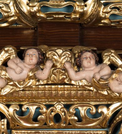 Zdjęcie nr 45: Ołtarz architektoniczny, dwukondygnacyjny, jednoosiowy ze zwieńczeniem. Mensa prostopadłościenna, antepedium w kształcie leżącego prostokąta, flankowane dwoma kanelowanymi pilastrami. W polu, w złoconej ramie dwie połączone płyciny w kształcie stojącego prostokąta wypełnione symetryczną dekoracją z akantu na błękitnym tle. Tabernakulum w formie prostopadłościennej, marmurowej skrzynki, zamknięte od góry prostym, złoconym gzymsem. Ścianka frontowa i drzwiczki obwiedzione złoconymi listwami, w polu łaciński krzyż. Cokół nastawy ustawiony na jednym stopniu, pośrodku zdobiony płyciną w kształcie leżącego prostokąta o zaokrąglonych krótszych bokach, imposty dekorowane mniejszymi płycinami wypełnionymi dekoracją roślinną. Pierwsza kondygnacja ujęta parą kolumn dźwigających przerwane belkowanie z przyczółkami, po bokach dodatkowo flankowana uszami wykończonymi ornamentem małżowinowo-chrząstkowym. W polu głównym obraz Matki Boskiej Szkaplerznej oraz św. Józefa z Dzieciątkiem i ze św. Janem Chrzcicielem na zasuwie, nad nimi para, małych uskrzydlonych aniołków. Po bokach nastawy dwie rzeźby: po prawej św. Katarzyna Aleksandryjska, a po lewej św. Barbara. Na przyczółkach usadzone dwie rzeźby aniołów z rozłożonymi szeroko rękami. Kolumny ustawione na tle prostokątnych płycin, z bazami, trzony gładkie, kapitele kompozytowe. Druga kondygnacja flankowana parą kolumn podtrzymujących wyłamane belkowanie. W polu, w ramie o kształcie stojącego prostokąta o ściętych narożach obraz św. Katarzyny Aleksandryjskiej. W zwieńczeniu promienista gloria z monogramem Marii na błękitnym tle, obwiedzionym wieńcem z obłoków. Struktura malowana w kolorze naturalnego drewna, ornamentyka złocona, detale srebrzone i błękitne.

