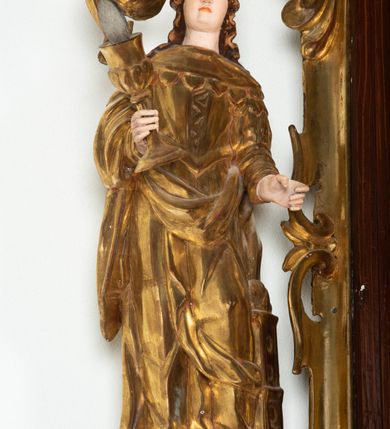 Zdjęcie nr 49: Ołtarz architektoniczny, dwukondygnacyjny, jednoosiowy ze zwieńczeniem. Mensa prostopadłościenna, antepedium w kształcie leżącego prostokąta, flankowane dwoma kanelowanymi pilastrami. W polu, w złoconej ramie dwie połączone płyciny w kształcie stojącego prostokąta wypełnione symetryczną dekoracją z akantu na błękitnym tle. Tabernakulum w formie prostopadłościennej, marmurowej skrzynki, zamknięte od góry prostym, złoconym gzymsem. Ścianka frontowa i drzwiczki obwiedzione złoconymi listwami, w polu łaciński krzyż. Cokół nastawy ustawiony na jednym stopniu, pośrodku zdobiony płyciną w kształcie leżącego prostokąta o zaokrąglonych krótszych bokach, imposty dekorowane mniejszymi płycinami wypełnionymi dekoracją roślinną. Pierwsza kondygnacja ujęta parą kolumn dźwigających przerwane belkowanie z przyczółkami, po bokach dodatkowo flankowana uszami wykończonymi ornamentem małżowinowo-chrząstkowym. W polu głównym obraz Matki Boskiej Szkaplerznej oraz św. Józefa z Dzieciątkiem i ze św. Janem Chrzcicielem na zasuwie, nad nimi para, małych uskrzydlonych aniołków. Po bokach nastawy dwie rzeźby: po prawej św. Katarzyna Aleksandryjska, a po lewej św. Barbara. Na przyczółkach usadzone dwie rzeźby aniołów z rozłożonymi szeroko rękami. Kolumny ustawione na tle prostokątnych płycin, z bazami, trzony gładkie, kapitele kompozytowe. Druga kondygnacja flankowana parą kolumn podtrzymujących wyłamane belkowanie. W polu, w ramie o kształcie stojącego prostokąta o ściętych narożach obraz św. Katarzyny Aleksandryjskiej. W zwieńczeniu promienista gloria z monogramem Marii na błękitnym tle, obwiedzionym wieńcem z obłoków. Struktura malowana w kolorze naturalnego drewna, ornamentyka złocona, detale srebrzone i błękitne.

