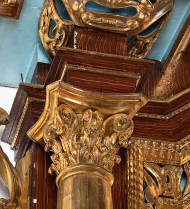 Zdjęcie nr 52: Ołtarz architektoniczny, dwukondygnacyjny, jednoosiowy ze zwieńczeniem. Mensa prostopadłościenna, antepedium w kształcie leżącego prostokąta, flankowane dwoma kanelowanymi pilastrami. W polu, w złoconej ramie dwie połączone płyciny w kształcie stojącego prostokąta wypełnione symetryczną dekoracją z akantu na błękitnym tle. Tabernakulum w formie prostopadłościennej, marmurowej skrzynki, zamknięte od góry prostym, złoconym gzymsem. Ścianka frontowa i drzwiczki obwiedzione złoconymi listwami, w polu łaciński krzyż. Cokół nastawy ustawiony na jednym stopniu, pośrodku zdobiony płyciną w kształcie leżącego prostokąta o zaokrąglonych krótszych bokach, imposty dekorowane mniejszymi płycinami wypełnionymi dekoracją roślinną. Pierwsza kondygnacja ujęta parą kolumn dźwigających przerwane belkowanie z przyczółkami, po bokach dodatkowo flankowana uszami wykończonymi ornamentem małżowinowo-chrząstkowym. W polu głównym obraz Matki Boskiej Szkaplerznej oraz św. Józefa z Dzieciątkiem i ze św. Janem Chrzcicielem na zasuwie, nad nimi para, małych uskrzydlonych aniołków. Po bokach nastawy dwie rzeźby: po prawej św. Katarzyna Aleksandryjska, a po lewej św. Barbara. Na przyczółkach usadzone dwie rzeźby aniołów z rozłożonymi szeroko rękami. Kolumny ustawione na tle prostokątnych płycin, z bazami, trzony gładkie, kapitele kompozytowe. Druga kondygnacja flankowana parą kolumn podtrzymujących wyłamane belkowanie. W polu, w ramie o kształcie stojącego prostokąta o ściętych narożach obraz św. Katarzyny Aleksandryjskiej. W zwieńczeniu promienista gloria z monogramem Marii na błękitnym tle, obwiedzionym wieńcem z obłoków. Struktura malowana w kolorze naturalnego drewna, ornamentyka złocona, detale srebrzone i błękitne.

