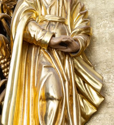 Zdjęcie nr 7: Nastawa ołtarzowa architektoniczna, jednokondygnacyjna i jednoosiowa. Ołtarz prostopadłościenny, mensa drewniana z kamiennym portatylem. Cokół nastawy ustawiony na ołtarzu pośrodku zdobiony płyciną w kształcie leżącego prostokąta o zaokrąglonych krótszych bokach, imposty dekorowane rozetkami. Kondygnacja ujęta parą pięciobocznych pilastrów dźwigających przerwane belkowanie z przyczółkami, po bokach dodatkowo flankowana uszami wykończonymi ornamentem małżowinowo-chrząstkowym. Pilastry ustawione na bazach, mają kanelowane trzony i kompozytowe kapitele. W polu głównym w głębokiej wnęce umieszczony jest krucyfiks oraz rzeźba Matki Boskiej po lewej stronie i św. Jana Ewangelisty po prawej. Tło wyłożono tkaniną. Po bokach krucyfiksu zawieszone są dwa gorejące serca na tle promienistej glorii. Obramienie wnęki wykończone ażurową wicią winorośli po bokach, a w łuku podwieszonymi szyszkami. Nad wnęką uskrzydlona główka aniołka z szyją podwiązaną chustą, skierowana na wprost. Analogiczne rzeźby znajdują się w partii fryzu na osi kolumn. Na przyczółkach ułożona jest para aniołków z arma Christi w dłoniach. W zwieńczeniu promienista gloria z monogramem Chrystusa na czerwonym tle, obwiedzionym wieńcem z obłoków. Struktura malowana w kolorze naturalnego drewna, ornamentyka złocona, detale czerwone.
