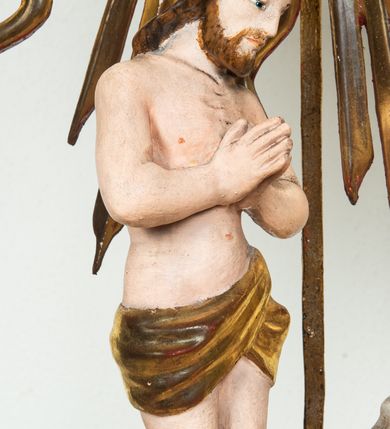 Zdjęcie nr 7: Pokrywa chrzcielnicy na planie koła z dekoracją imitującą puklowanie. Na szczycie pokrywy umieszczona rzeźbiona scena przedstawiająca Chrzest Chrystusa w Jordanie. Po lewej stronie Jezus stopami zanurzony w wodach Jordanu, zwrócony trzy czwarte w stronę św. Jana Chrzciciela, z rękami złożonymi na piersiach w geście pokory. Twarz podłużna, okolona brodą z długim nosem i wzrokiem skierowanym w dół. Włosy długie, opadające na plecy. Ubrany jest w złocone perizonium, luźno zawiązane na biodrach. Po prawej św. Jan Chrzciciel klęczący na kamiennym postumencie, zwrócony w prawo, w lewej ręce trzymający krzyż, prawą polewający wodą Chrystusa. Twarz podłużna, okolona krótką brodą i długimi włosami. Ubrany jest w skórę wielbłądzią, odsłaniającą nagi tors i nogi. Krzyż długi z napisem na banderoli: „OTO BARANEK BOŻY”. Za nimi zatknięta jest duża, promienista gloria, pośrodku której znajduje się gołębica Ducha Świętego, a nad nią półpostać Boga Ojca wynurzająca się z obłoków z rozłożonymi szeroko rękami. Bóg Ojciec o rysach twarzy starszego mężczyzny z siwymi włosami i brodą, ubrany w złoconą suknię. Polichromia w odsłoniętych partiach ciała naturalistyczna, podstawa pokrywy, gloria i szaty złocone, obłoki srebrzone.


