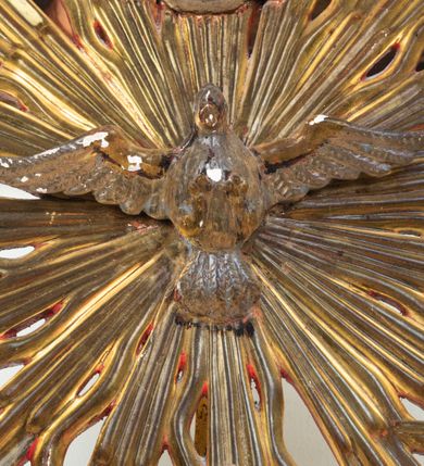 Zdjęcie nr 8: Pokrywa chrzcielnicy na planie koła z dekoracją imitującą puklowanie. Na szczycie pokrywy umieszczona rzeźbiona scena przedstawiająca Chrzest Chrystusa w Jordanie. Po lewej stronie Jezus stopami zanurzony w wodach Jordanu, zwrócony trzy czwarte w stronę św. Jana Chrzciciela, z rękami złożonymi na piersiach w geście pokory. Twarz podłużna, okolona brodą z długim nosem i wzrokiem skierowanym w dół. Włosy długie, opadające na plecy. Ubrany jest w złocone perizonium, luźno zawiązane na biodrach. Po prawej św. Jan Chrzciciel klęczący na kamiennym postumencie, zwrócony w prawo, w lewej ręce trzymający krzyż, prawą polewający wodą Chrystusa. Twarz podłużna, okolona krótką brodą i długimi włosami. Ubrany jest w skórę wielbłądzią, odsłaniającą nagi tors i nogi. Krzyż długi z napisem na banderoli: „OTO BARANEK BOŻY”. Za nimi zatknięta jest duża, promienista gloria, pośrodku której znajduje się gołębica Ducha Świętego, a nad nią półpostać Boga Ojca wynurzająca się z obłoków z rozłożonymi szeroko rękami. Bóg Ojciec o rysach twarzy starszego mężczyzny z siwymi włosami i brodą, ubrany w złoconą suknię. Polichromia w odsłoniętych partiach ciała naturalistyczna, podstawa pokrywy, gloria i szaty złocone, obłoki srebrzone.


