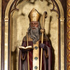 Zdjęcie nr 1: Rzeźba przedstawia św. Wojciecha, ukazanego frontalnie w postawie stojącej. Święty w lewej ręce trzyma pastorał, a w prawej otwartą księgę, o prawe ramię ma oparte wiosło. Twarz szczupła o wyraźnie wystających kościach policzkowych, otwartych ustach, krótkim nosie i wzroku skierowanym na wprost. Głowę okalają długie, siwe i falowane włosy oraz długa broda. Święty jest ubrany w żółtą albę, białą komżę zdobioną u dołu złotym pasem, bordowy ornat i rękawice, złoty paliusz oraz złotą infułę na głowie. Rzeźba ustawiona jest na niskim, brązowym, prostopadłościennym cokole. Polichromia w odsłoniętych partiach ciała naturalistyczna, atrybuty i detale złocone.

