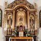 Zdjęcie nr 1: Rzeźba przedstawia św. Stanisława, ukazanego frontalnie w postawie stojącej. Święty w lewej ręce trzyma pastorał, a prawą ugiętą w łokciu wyciąga przed siebie. Twarz owalna o dużych ustach i nosie, wzroku skierowanym na wprost. Głowę okalają średniej długości włosy, silnie skręcone, zasłaniające uszy. Święty jest ubrany w żółtą albę, białą komżę zdobioną u dołu złotym pasem, bordowy ornat i rękawice, złoty paliusz oraz złotą infułę na głowie. U dołu po prawej stronie widoczny jest w półpostaci i z lewego profilu Piotrowin z lewą ręką uniesioną do góry. Ubrany jest w białą tkaninę nałożoną na głowę. Rzeźby ustawione są na niskim, brązowym, prostopadłościennym cokole. Polichromia w odsłoniętych partiach ciała naturalistyczna, atrybuty i detale złocone.
