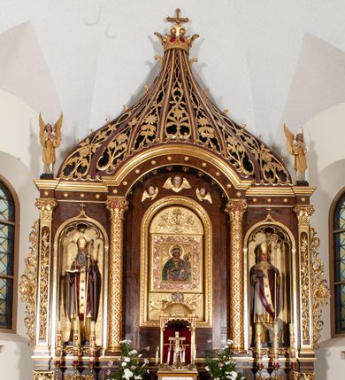 Zdjęcie nr 1: Rzeźba przedstawia św. Stanisława, ukazanego frontalnie w postawie stojącej. Święty w lewej ręce trzyma pastorał, a prawą ugiętą w łokciu wyciąga przed siebie. Twarz owalna o dużych ustach i nosie, wzroku skierowanym na wprost. Głowę okalają średniej długości włosy, silnie skręcone, zasłaniające uszy. Święty jest ubrany w żółtą albę, białą komżę zdobioną u dołu złotym pasem, bordowy ornat i rękawice, złoty paliusz oraz złotą infułę na głowie. U dołu po prawej stronie widoczny jest w półpostaci i z lewego profilu Piotrowin z lewą ręką uniesioną do góry. Ubrany jest w białą tkaninę nałożoną na głowę. Rzeźby ustawione są na niskim, brązowym, prostopadłościennym cokole. Polichromia w odsłoniętych partiach ciała naturalistyczna, atrybuty i detale złocone.
