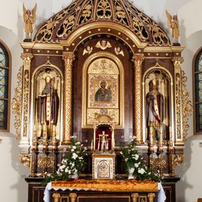 Zdjęcie nr 1: Rzeźba przedstawia św. Stanisława, ukazanego frontalnie w postawie stojącej. Święty w lewej ręce trzyma pastorał, a prawą ugiętą w łokciu wyciąga przed siebie. Twarz owalna o dużych ustach i nosie, wzroku skierowanym na wprost. Głowę okalają średniej długości włosy, silnie skręcone, zasłaniające uszy. Święty jest ubrany w żółtą albę, białą komżę zdobioną u dołu złotym pasem, bordowy ornat i rękawice, złoty paliusz oraz złotą infułę na głowie. U dołu po prawej stronie widoczny jest w półpostaci i z lewego profilu Piotrowin z lewą ręką uniesioną do góry. Ubrany jest w białą tkaninę nałożoną na głowę. Rzeźby ustawione są na niskim, brązowym, prostopadłościennym cokole. Polichromia w odsłoniętych partiach ciała naturalistyczna, atrybuty i detale złocone.
