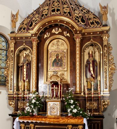 Zdjęcie nr 2: Rzeźba przedstawia św. Stanisława, ukazanego frontalnie w postawie stojącej. Święty w lewej ręce trzyma pastorał, a prawą ugiętą w łokciu wyciąga przed siebie. Twarz owalna o dużych ustach i nosie, wzroku skierowanym na wprost. Głowę okalają średniej długości włosy, silnie skręcone, zasłaniające uszy. Święty jest ubrany w żółtą albę, białą komżę zdobioną u dołu złotym pasem, bordowy ornat i rękawice, złoty paliusz oraz złotą infułę na głowie. U dołu po prawej stronie widoczny jest w półpostaci i z lewego profilu Piotrowin z lewą ręką uniesioną do góry. Ubrany jest w białą tkaninę nałożoną na głowę. Rzeźby ustawione są na niskim, brązowym, prostopadłościennym cokole. Polichromia w odsłoniętych partiach ciała naturalistyczna, atrybuty i detale złocone.
