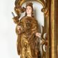 Zdjęcie nr 1: Rzeźba przedstawiająca św. Barbarę, ustawiona na niskim cokole. Święta ukazana frontalnie w delikatnym kontrapoście, z kielichem z hostią w prawej dłoni oraz lewą ręką ugiętą w łokciu i wyciągniętą przed siebie. Twarz owalna z małymi ustami, długim i szerokim nosem, migdałowymi oczami. Włosy długie, brązowe, opadające falami na plecy. Święta ubrana jest w złotą, długą suknię z długimi rękawami oraz złoty płaszcz, na stopach ma założone buty, a na głowę otwartą koronę. Po jej lewej stronie ustawiona jest miniaturowa, dwukondygnacyjna wieża z prostokątnym otworem drzwiowym i trzema okrągłymi oknami, zamknięta kopułą. Kielich na okrągłej stopie, z trzonem przechodzącym w wąską tuleję, oddzieloną od czary półkolistym talerzykiem, czara w dolnej części zdobiona puklowaniem. Polichromia w odsłoniętych partiach ciała naturalistyczna, szaty i atrybuty złocone i srebrzone, detale błękitne (wnętrze korony i monogram na hostii).




