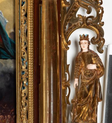 Zdjęcie nr 2: Rzeźba przedstawiająca św. Katarzynę Aleksandryjską, ustawiona na niskim cokole. Święta ukazana frontalnie w delikatnym kontrapoście, z sylwetką przechyloną w prawą stronę, z lewą ręką złożoną na tułowiu, a prawą opartą o złamane koło. Twarz owalna z małymi ustami, długim i wąskim nosem, migdałowymi oczami. Włosy długie, brązowe, opadające falami na plecy i wzdłuż ramion. Święta ubrana jest w złotą, długą suknię z długimi rękawami oraz złoty płaszcz, na stopach ma założone buty, a na głowę otwartą koronę. Polichromia w odsłoniętych partiach ciała naturalistyczna, szaty i atrybuty złocone i srebrzone, detale błękitne (wnętrze korony).



