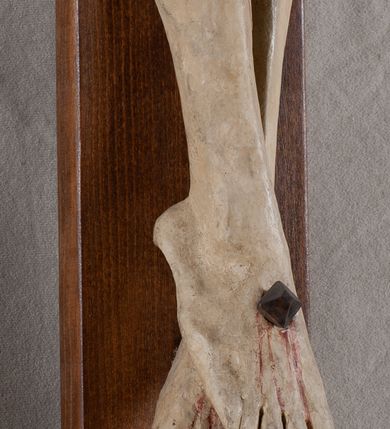 Zdjęcie nr 5: Rzeźba Chrystusa przybita do krzyża trzema gwoździami, pełna. Zbawiciel ukazany w typie Cristo morte, w lekkim zwisie, z głową pochyloną na prawą stronę. Jezus ma szczupłą sylwetkę ciała, duże stopy, delikatnie podkreśloną linię żeber. Jego twarz jest podłużna, ma długi nos, delikatnie otwarte usta i zamknięte oczy, krótką brodę, zwiniętą na końcu w dwa pukle. Ma długie, brązowe włosy spływające falami do przodu, a na głowie założoną koronę cierniową złożoną z prostych zielonych gałązek. Biodra oplata złocone perizonium z zieloną podszewką, zawiązane pośrodku. Z dłoni, stóp i boku Chrystusa spływają strużki krwi. Polichromia ciała naturalistyczna, perizonium złocone. Nad głową Jezusa titulus w formie banderoli z napisem „I. N. R. I.”. Krzyż prosty, gładki, malowany na brązowo.
