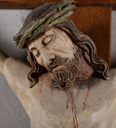Zdjęcie nr 2: Rzeźba Chrystusa przybita do krzyża trzema gwoździami, pełna. Zbawiciel ukazany w typie Cristo morte, w lekkim zwisie, z głową pochyloną na prawą stronę. Jezus ma szczupłą sylwetkę ciała, duże stopy, delikatnie podkreśloną linię żeber. Jego twarz jest podłużna, ma długi nos, delikatnie otwarte usta i zamknięte oczy, krótką brodę, zwiniętą na końcu w dwa pukle. Ma długie, brązowe włosy spływające falami do przodu, a na głowie założoną koronę cierniową złożoną z prostych zielonych gałązek. Biodra oplata złocone perizonium z zieloną podszewką, zawiązane pośrodku. Z dłoni, stóp i boku Chrystusa spływają strużki krwi. Polichromia ciała naturalistyczna, perizonium złocone. Nad głową Jezusa titulus w formie banderoli z napisem „I. N. R. I.”. Krzyż prosty, gładki, malowany na brązowo.
