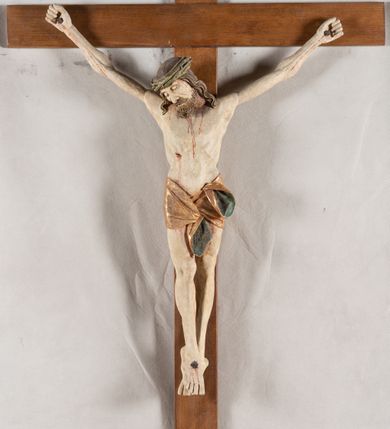 Zdjęcie nr 9: Rzeźba Chrystusa przybita do krzyża trzema gwoździami, pełna. Zbawiciel ukazany w typie Cristo morte, w lekkim zwisie, z głową pochyloną na prawą stronę. Jezus ma szczupłą sylwetkę ciała, duże stopy, delikatnie podkreśloną linię żeber. Jego twarz jest podłużna, ma długi nos, delikatnie otwarte usta i zamknięte oczy, krótką brodę, zwiniętą na końcu w dwa pukle. Ma długie, brązowe włosy spływające falami do przodu, a na głowie założoną koronę cierniową złożoną z prostych zielonych gałązek. Biodra oplata złocone perizonium z zieloną podszewką, zawiązane pośrodku. Z dłoni, stóp i boku Chrystusa spływają strużki krwi. Polichromia ciała naturalistyczna, perizonium złocone. Nad głową Jezusa titulus w formie banderoli z napisem „I. N. R. I.”. Krzyż prosty, gładki, malowany na brązowo.
