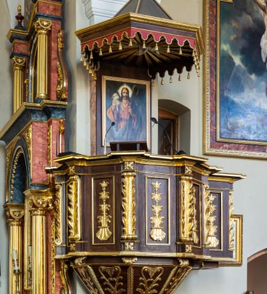 Zdjęcie nr 1: Ambona wisząca, przyścienna, z wejściem prowadzącym od zakrystii. 
Kosz na planie sześcioboku z podwieszeniem w postaci sześciobocznego stożka zakończonego szyszką. Ścianki kosza flankowane pilastrami podtrzymującymi niepełne belkowanie, zamknięte gzymsem wyłamanym na osi podpór tworzące parapet ambony. Ścianki podstawy dekorowane fantazyjną wicią roślinną złożoną ze stylizowanych liści akantu i kampanul. Ścianki kosza ozdobione prostokątnymi płycinami w złoconych, profilowanych ramach; w polu dekorowane stylizowaną, pionową wicią utworzoną z kampanul wyrastających z muszli. Pilastry ustawione na niskich cokolikach zdobionych rozetami, z trzonami z szerokim pasem utworzonym z liści o ostrych zakończeniach. 

W zaplecku, w prostokątnej ramie współczesny obraz Jezusa Dobrego Pasterza, namalowany  przez Zbigniewa Juszczaka. 
Baldachim na planie sześcioboku od dołu zdobiony lambrekinem, zamknięty od góry profilowanym gzymsem, w zwieńczeniu z bogato dekorowanym krzyżem łacińskim stojącym na ostrosłupie. U spodu baldachimu gołębica Ducha Świętego na tle promieni ułożonych w wiązki o nierównej długości. 
Struktura polichromowana na kolor ciemnobrązowy, ornamentyka i profilowania złocone.
