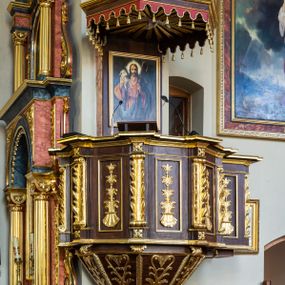 Zdjęcie nr 1: Ambona wisząca, przyścienna, z wejściem prowadzącym od zakrystii. 
Kosz na planie sześcioboku z podwieszeniem w postaci sześciobocznego stożka zakończonego szyszką. Ścianki kosza flankowane pilastrami podtrzymującymi niepełne belkowanie, zamknięte gzymsem wyłamanym na osi podpór tworzące parapet ambony. Ścianki podstawy dekorowane fantazyjną wicią roślinną złożoną ze stylizowanych liści akantu i kampanul. Ścianki kosza ozdobione prostokątnymi płycinami w złoconych, profilowanych ramach; w polu dekorowane stylizowaną, pionową wicią utworzoną z kampanul wyrastających z muszli. Pilastry ustawione na niskich cokolikach zdobionych rozetami, z trzonami z szerokim pasem utworzonym z liści o ostrych zakończeniach. 

W zaplecku, w prostokątnej ramie współczesny obraz Jezusa Dobrego Pasterza, namalowany  przez Zbigniewa Juszczaka. 
Baldachim na planie sześcioboku od dołu zdobiony lambrekinem, zamknięty od góry profilowanym gzymsem, w zwieńczeniu z bogato dekorowanym krzyżem łacińskim stojącym na ostrosłupie. U spodu baldachimu gołębica Ducha Świętego na tle promieni ułożonych w wiązki o nierównej długości. 
Struktura polichromowana na kolor ciemnobrązowy, ornamentyka i profilowania złocone.
