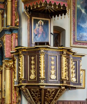 Zdjęcie nr 1: Ambona wisząca, przyścienna, z wejściem prowadzącym od zakrystii. 
Kosz na planie sześcioboku z podwieszeniem w postaci sześciobocznego stożka zakończonego szyszką. Ścianki kosza flankowane pilastrami podtrzymującymi niepełne belkowanie, zamknięte gzymsem wyłamanym na osi podpór tworzące parapet ambony. Ścianki podstawy dekorowane fantazyjną wicią roślinną złożoną ze stylizowanych liści akantu i kampanul. Ścianki kosza ozdobione prostokątnymi płycinami w złoconych, profilowanych ramach; w polu dekorowane stylizowaną, pionową wicią utworzoną z kampanul wyrastających z muszli. Pilastry ustawione na niskich cokolikach zdobionych rozetami, z trzonami z szerokim pasem utworzonym z liści o ostrych zakończeniach. 

W zaplecku, w prostokątnej ramie współczesny obraz Jezusa Dobrego Pasterza, namalowany  przez Zbigniewa Juszczaka. 
Baldachim na planie sześcioboku od dołu zdobiony lambrekinem, zamknięty od góry profilowanym gzymsem, w zwieńczeniu z bogato dekorowanym krzyżem łacińskim stojącym na ostrosłupie. U spodu baldachimu gołębica Ducha Świętego na tle promieni ułożonych w wiązki o nierównej długości. 
Struktura polichromowana na kolor ciemnobrązowy, ornamentyka i profilowania złocone.
