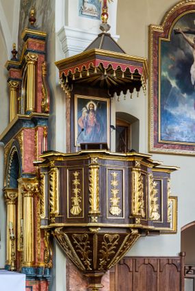 Zdjęcie nr 1: Ambona wisząca, przyścienna, z wejściem prowadzącym od zakrystii. 
Kosz na planie sześcioboku z podwieszeniem w postaci sześciobocznego stożka zakończonego szyszką. Ścianki kosza flankowane pilastrami podtrzymującymi niepełne belkowanie, zamknięte gzymsem wyłamanym na osi podpór tworzące parapet ambony. Ścianki podstawy dekorowane fantazyjną wicią roślinną złożoną ze stylizowanych liści akantu i kampanul. Ścianki kosza ozdobione prostokątnymi płycinami w złoconych, profilowanych ramach; w polu dekorowane stylizowaną, pionową wicią utworzoną z kampanul wyrastających z muszli. Pilastry ustawione na niskich cokolikach zdobionych rozetami, z trzonami z szerokim pasem utworzonym z liści o ostrych zakończeniach. 

W zaplecku, w prostokątnej ramie współczesny obraz Jezusa Dobrego Pasterza, namalowany  przez Zbigniewa Juszczaka. 
Baldachim na planie sześcioboku od dołu zdobiony lambrekinem, zamknięty od góry profilowanym gzymsem, w zwieńczeniu z bogato dekorowanym krzyżem łacińskim stojącym na ostrosłupie. U spodu baldachimu gołębica Ducha Świętego na tle promieni ułożonych w wiązki o nierównej długości. 
Struktura polichromowana na kolor ciemnobrązowy, ornamentyka i profilowania złocone.
