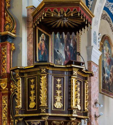 Zdjęcie nr 3: Ambona wisząca, przyścienna, z wejściem prowadzącym od zakrystii. 
Kosz na planie sześcioboku z podwieszeniem w postaci sześciobocznego stożka zakończonego szyszką. Ścianki kosza flankowane pilastrami podtrzymującymi niepełne belkowanie, zamknięte gzymsem wyłamanym na osi podpór tworzące parapet ambony. Ścianki podstawy dekorowane fantazyjną wicią roślinną złożoną ze stylizowanych liści akantu i kampanul. Ścianki kosza ozdobione prostokątnymi płycinami w złoconych, profilowanych ramach; w polu dekorowane stylizowaną, pionową wicią utworzoną z kampanul wyrastających z muszli. Pilastry ustawione na niskich cokolikach zdobionych rozetami, z trzonami z szerokim pasem utworzonym z liści o ostrych zakończeniach. 

W zaplecku, w prostokątnej ramie współczesny obraz Jezusa Dobrego Pasterza, namalowany  przez Zbigniewa Juszczaka. 
Baldachim na planie sześcioboku od dołu zdobiony lambrekinem, zamknięty od góry profilowanym gzymsem, w zwieńczeniu z bogato dekorowanym krzyżem łacińskim stojącym na ostrosłupie. U spodu baldachimu gołębica Ducha Świętego na tle promieni ułożonych w wiązki o nierównej długości. 
Struktura polichromowana na kolor ciemnobrązowy, ornamentyka i profilowania złocone.
