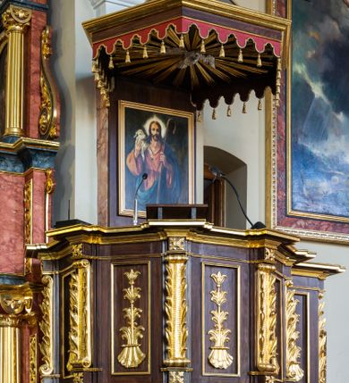 Zdjęcie nr 4: Ambona wisząca, przyścienna, z wejściem prowadzącym od zakrystii. 
Kosz na planie sześcioboku z podwieszeniem w postaci sześciobocznego stożka zakończonego szyszką. Ścianki kosza flankowane pilastrami podtrzymującymi niepełne belkowanie, zamknięte gzymsem wyłamanym na osi podpór tworzące parapet ambony. Ścianki podstawy dekorowane fantazyjną wicią roślinną złożoną ze stylizowanych liści akantu i kampanul. Ścianki kosza ozdobione prostokątnymi płycinami w złoconych, profilowanych ramach; w polu dekorowane stylizowaną, pionową wicią utworzoną z kampanul wyrastających z muszli. Pilastry ustawione na niskich cokolikach zdobionych rozetami, z trzonami z szerokim pasem utworzonym z liści o ostrych zakończeniach. 

W zaplecku, w prostokątnej ramie współczesny obraz Jezusa Dobrego Pasterza, namalowany  przez Zbigniewa Juszczaka. 
Baldachim na planie sześcioboku od dołu zdobiony lambrekinem, zamknięty od góry profilowanym gzymsem, w zwieńczeniu z bogato dekorowanym krzyżem łacińskim stojącym na ostrosłupie. U spodu baldachimu gołębica Ducha Świętego na tle promieni ułożonych w wiązki o nierównej długości. 
Struktura polichromowana na kolor ciemnobrązowy, ornamentyka i profilowania złocone.
