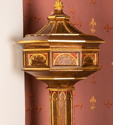 Zdjęcie nr 1: Chrzcielnica na podstawie na planie pięciu boków z ośmioboku. Stopa ośmioboczna zakończona takimże talerzykiem. Trzon ośmioboczny, dekorowany ostrołukowymi blendami z prostym maswerkiem. Czara ośmioboczna, spłaszczona, jej ścianki dekorowane płycinami z półkolistymi łukami i maswerkiem. Pokrywa ośmioboczna zwężająca się ku górze na kształt cokołu zwieńczonego krzyżem; ścianki dekorowane blendami. Chrzcielnica w kolorze naturalnego drewna; profile i ornamentyka złocone.