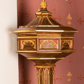 Zdjęcie nr 1: Chrzcielnica na podstawie na planie pięciu boków z ośmioboku. Stopa ośmioboczna zakończona takimże talerzykiem. Trzon ośmioboczny, dekorowany ostrołukowymi blendami z prostym maswerkiem. Czara ośmioboczna, spłaszczona, jej ścianki dekorowane płycinami z półkolistymi łukami i maswerkiem. Pokrywa ośmioboczna zwężająca się ku górze na kształt cokołu zwieńczonego krzyżem; ścianki dekorowane blendami. Chrzcielnica w kolorze naturalnego drewna; profile i ornamentyka złocone.